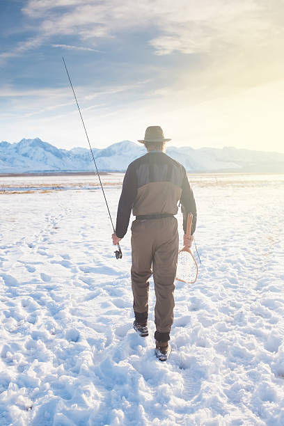 Fly Fisherman Hiking Across The Frozen Owens Valley Fly Fisherman Hiking Across The Frozen Owens Valley towards the river at sunset. owens river stock pictures, royalty-free photos & images