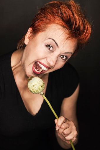 Mid adged woman with a funny facial expression holding an unripe poppy.