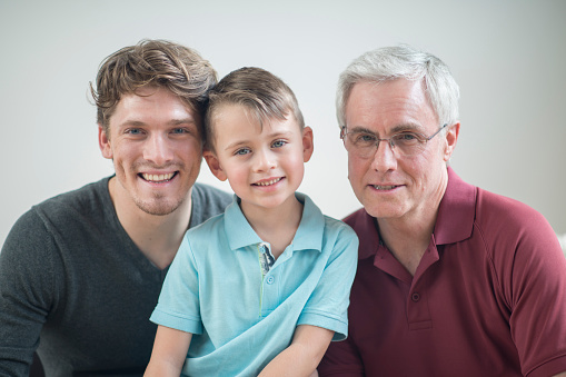 Three generations of men are sitting together and are smiling while looking at the camera.