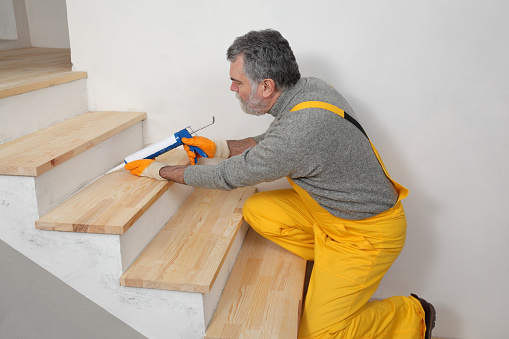 Construction worker caulking wooden stairs with silicone glue using cartridge, home renovation