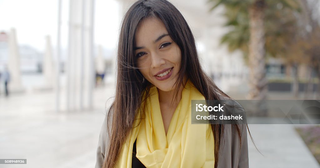 Joyful grinning woman outside in yellow scarf Single joyful grinning woman in yellow scarf standing outdoors need palm trees and buildings Adult Stock Photo