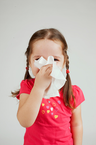 Little girl wipes her nose with a tissue.