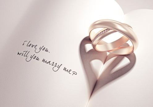 abstract wedding rings with heartshadow on a book middle with i love you will you marry me card text