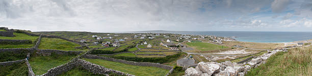 This image conveys the quietude of a Northern Irish harbor quayside, where maritime legacy meets the daily life of a coastal community. The weathered stone wall and the moored fishing vessels speak of a history rooted in the sea. An old building stands under renovation, symbolizing the ongoing story of the town and its people. The harbor water reflects the changing sky, a blend of blue and grey, where clouds race across the winter horizon. This scene, with its deep sense of place and the juxtaposition of past and present, offers a narrative-rich image that would be a compelling addition to any commercial image portfolio focusing on the rich tapestry of Ireland's coastal towns.