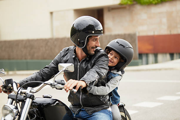 Father and son riding motorbike Happy father and son looking at each other while riding motorbike on street motorcycle stock pictures, royalty-free photos & images