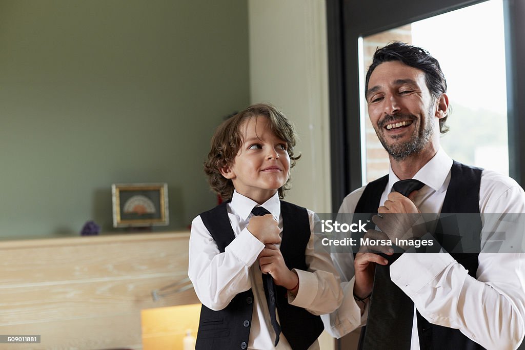 Boy adjusting tie while looking at father Cute little boy adjusting tie while looking at father in house Imitation Stock Photo
