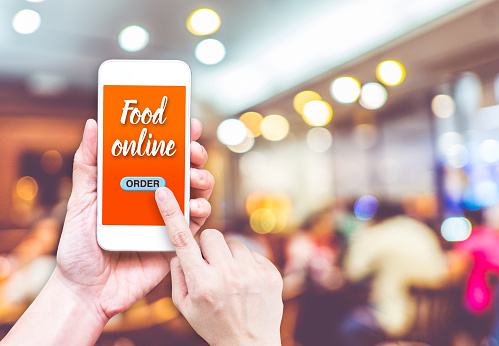 Hand holding mobile with Order food online with blur restaurant background, food online business concept.Leave space for adding your text.