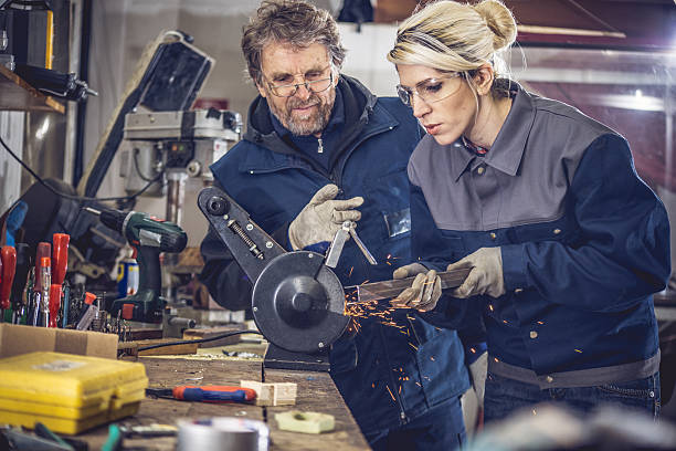 Young Woman Grinding Metal in Mechanical Workshop Young woman gridning metal in mechanical workshop, senior man supervising woman and teaching, employee training job retraining stock pictures, royalty-free photos & images