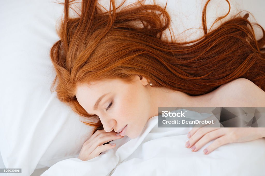 Tender woman with red hair sleeping in bed Tender cute young woman with long red hair lying and sleeping in bed Redhead Stock Photo