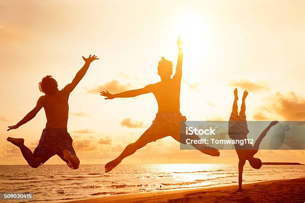 Young People Jumping On The Beach With Sunset Background Stock Photo - Download Image Now