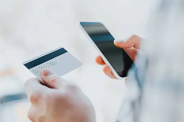 Photo of young man hands holding credit card and using phone