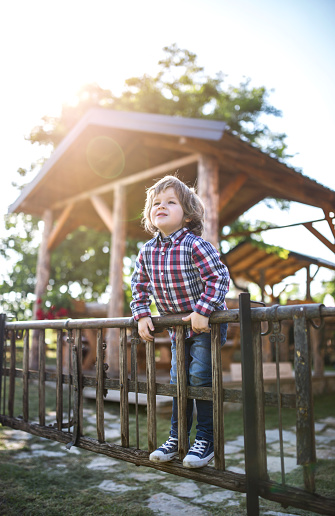 Cute little boy standing on wooden fence and looking away.