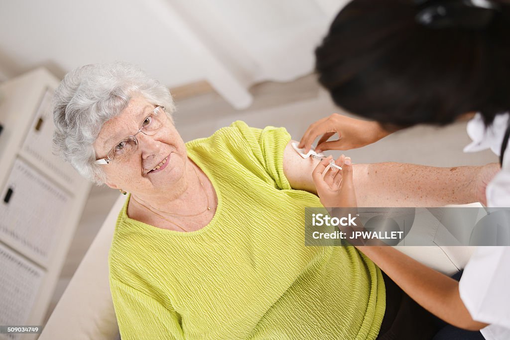 cheerful young nurse giving injection to elderly woman at home cheerful young nurse giving an injection to a elderly woman at home A Helping Hand Stock Photo