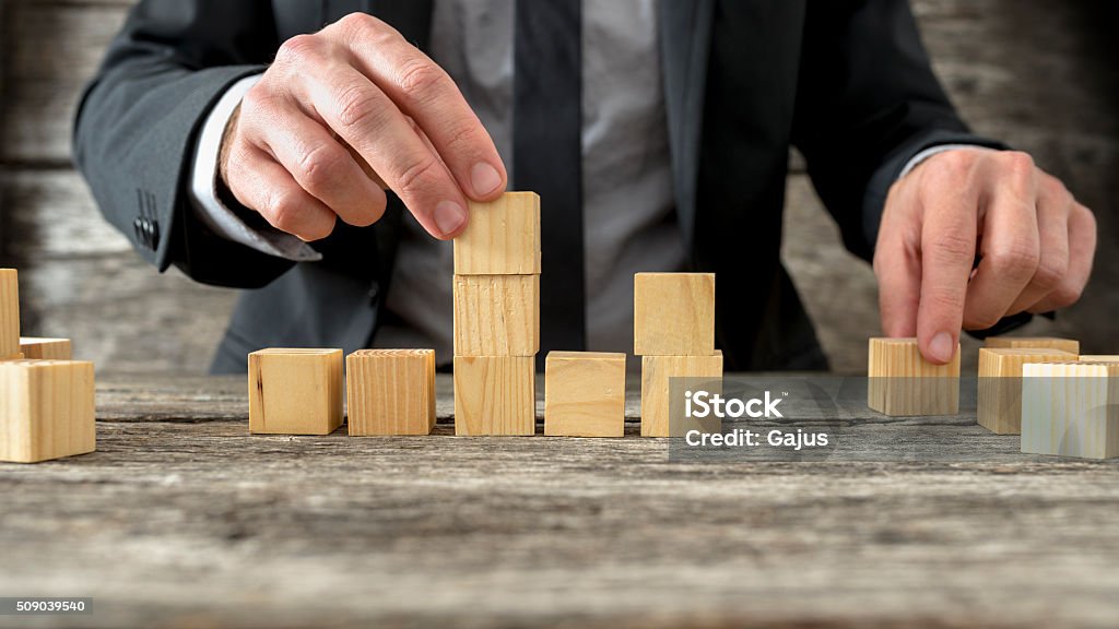 Concept of business strategy and planning Concept of business strategy and planning - front view of male hand placing and positioning wooden blocks in various structures. Toy Block Stock Photo