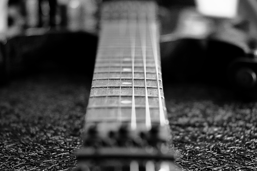 Black and white close up of senior man’s hand with fingers on the neck of an acoustic 12 string guitar.