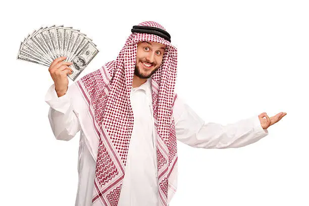 Young Arab spreading a stack of money and making a welcoming gesture with his hand isolated on white background