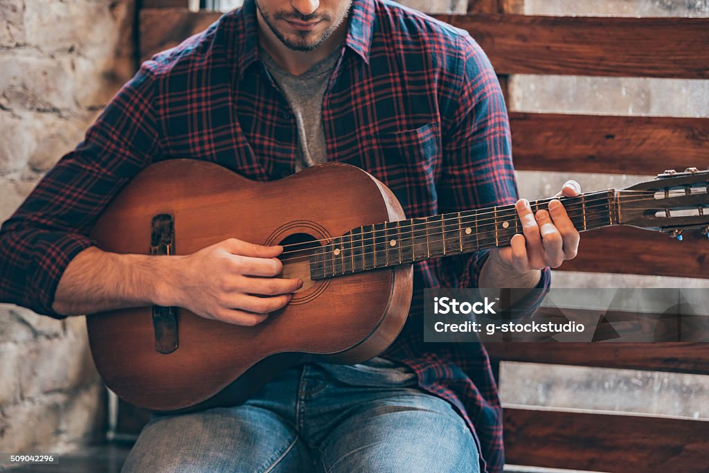 Playing perfect riff. Close-up part of young man playing guitar while sitting at windowsill Rustic Stock Photo