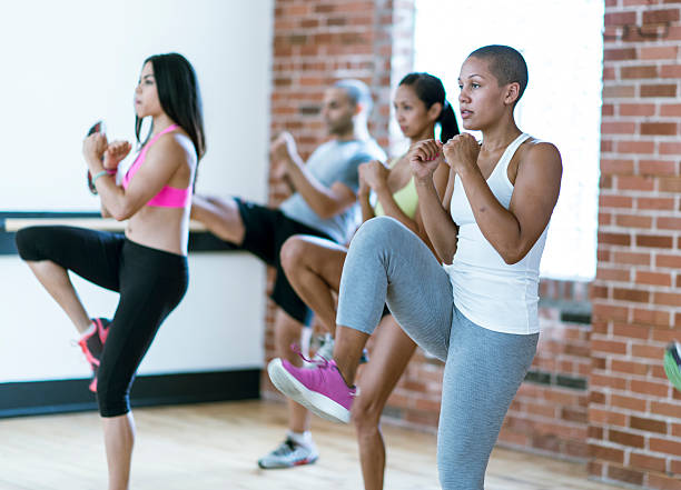 Taking a Kickboxing Class A multi-ethnic group of young adults are taking a kickboxing class together at the gym. kickboxing photos stock pictures, royalty-free photos & images