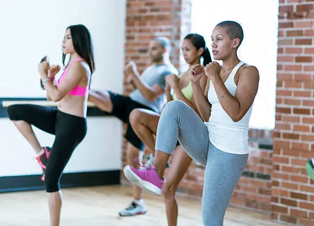 A multi-ethnic group of young adults are taking a kickboxing class together at the gym.
