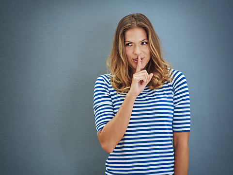 Studio shot of a young woman covering her lips with her finger against a gray backgroundhttp://195.154.178.81/DATA/i_collage/pi/shoots/806302.jpg