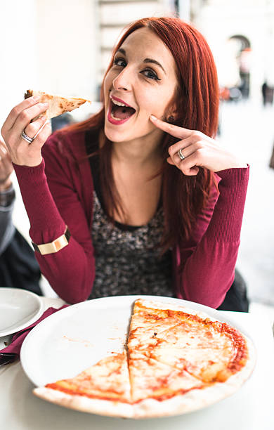 женщина ест пиццу в ресторане - italian culture women looking at camera cheerful стоковые фото и изображения