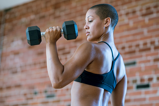 An athletic and muscular woman is lifting dumbbell weights at the gym.