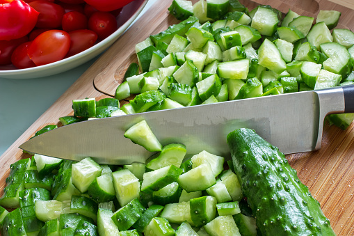sliced cucumbers on the cutting board and knife, in the background the tomatoes in a bowl