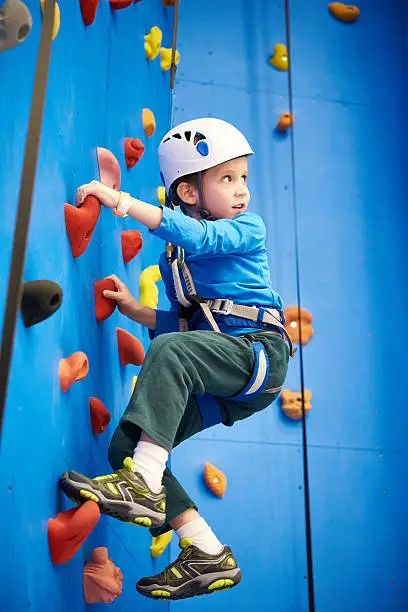 Little boy is climbing to amusement park on blue wall