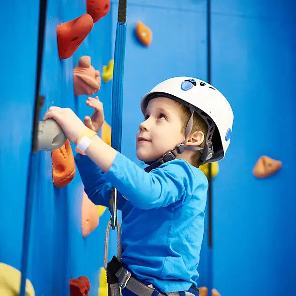 Little boy is climbing to amusement park on blue wall
