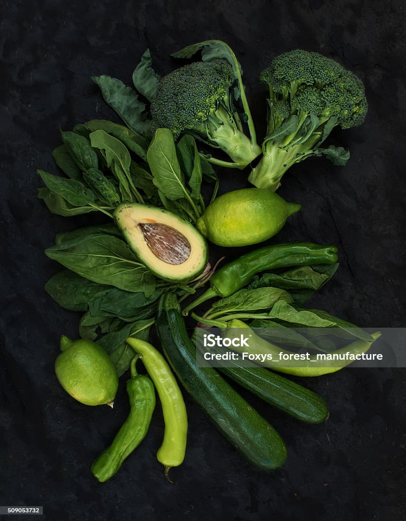 Raw green vegetables set. Broccoli, avocado, pepper, spinach, zuccini, lime Raw green vegetables set. Broccoli, avocado, pepper, spinach, zuccini, lime on  dark stone background, top view Avocado Stock Photo