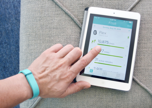 Vancouver, BC, Canada -- August 26, 2014:Close up of a man wearing a Fitbit Flex using the App on an iPad Mini.  The Fitbit Flex is a wireless activity and sleep monitor wristband that promotes activity and wellness.