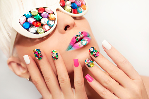 Makeup and manicure with multicolored crystals and glasses on the blonde girl.