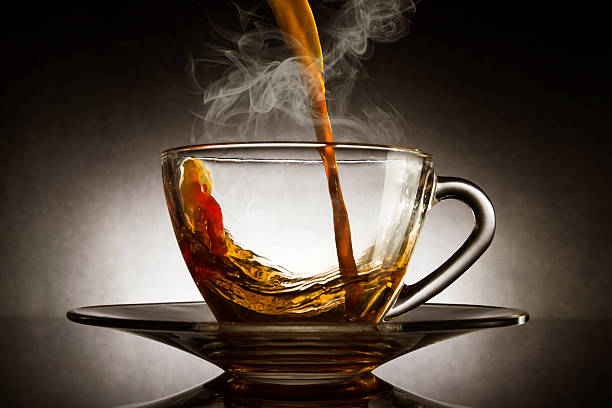Pour coffee into transparent glass cup with dark background.