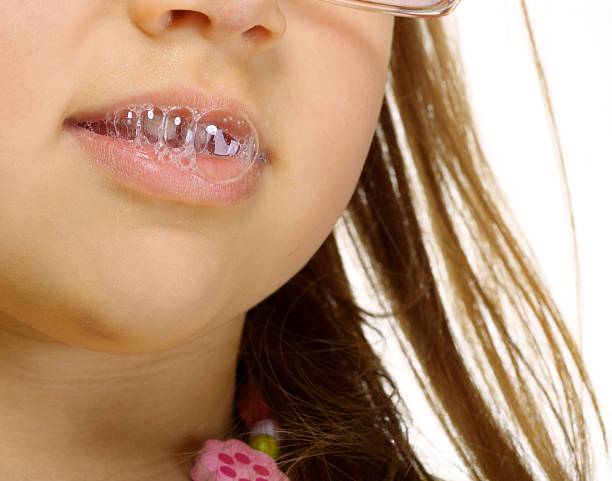 крупный план маленькая девочка в очки делать весело слюна bubbles - human saliva стоковые фото и изображения
