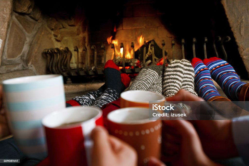 Friends sitting by the fireplace Four people warming their feet by the fireplace and drinking hot chocolate. Hot Chocolate Stock Photo