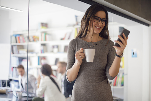 Women looking at smartphone, holding coffee cup