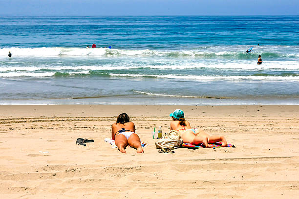 Ventura, CA, USA - June 30, 2015: Two young women sunbathing on Ventura beach whilst watching people swimming in the California pacific ocean