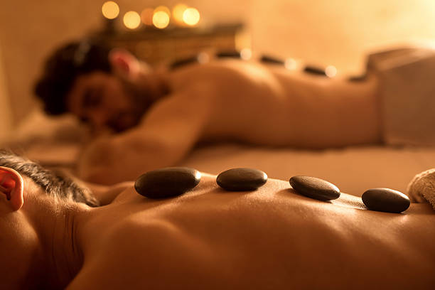 Unrecognizable woman receiving hot stone therapy at spa. Couple enjoying during spa treatment. Focus is on foreground, on unrecognizable woman receiving lastone therapy. hot stone massage stock pictures, royalty-free photos & images