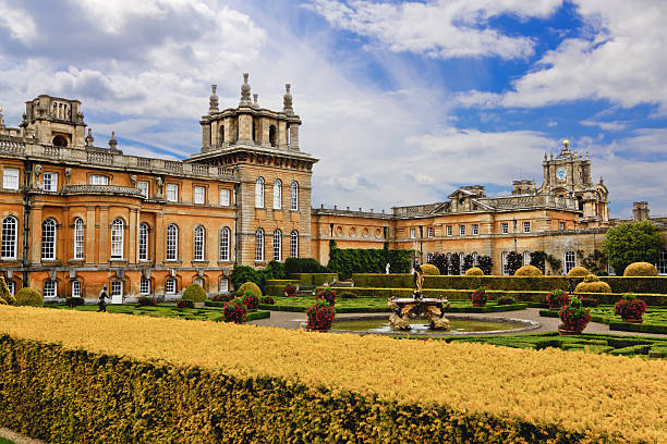 Blenheim Palace, Woodstock, Oxfordshire, England, United Kingdom. Woodstock, United Kingdom - June 27, 2015: Blenheim Palace, Woodstock, Oxfordshire, England. It is the principal residence of the dukes of Marlborough, and was built between 1705 and 1722. It is being used as a family home, mausoleum and national monument. The palace was also the birthplace of Sir Winston Churchill. Landscaped garden, yellow bushes, green grass and trees, flowers, fountain and blue sky with clouds are in the image. duke photos stock pictures, royalty-free photos & images
