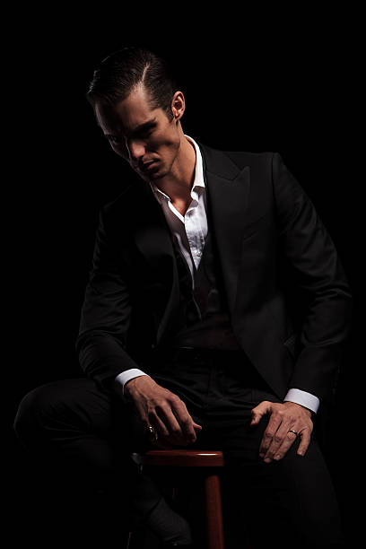 istock young businessman in black suit seated in dark studio 509100242