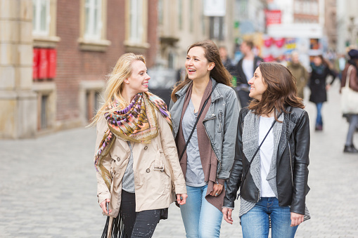 Group of women walking in Copenhagen. They are in their twenties and they are wearing smart casual clothes. Happiness and friendship concepts, they are smiling and looking each other.
