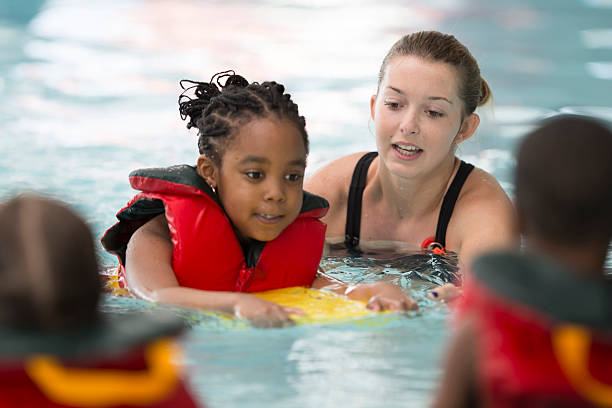 Swim Instructor Working with a Little Girl A multi-ethnic group of elementary age children are learning how to swim at the public pool. One little girl is holding onto a kick board and is swimming through the water. swimming stock pictures, royalty-free photos & images