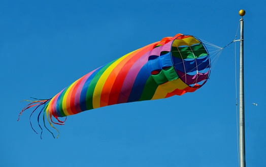 Bright colorful spinning windsock kite.  Wind sleeve is blowing in the ocean air breeze with blue sky background.