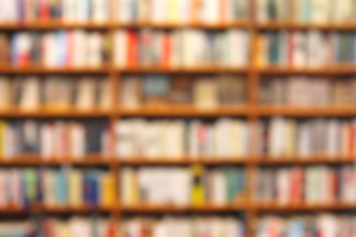 Defocused background of a bookstore, showing a brown bookcase with blurred shelves full of books with colored spines.