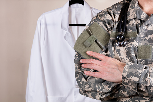 Close up partial view of medical doctor wearing military uniform and stethoscope with medical coat in background.