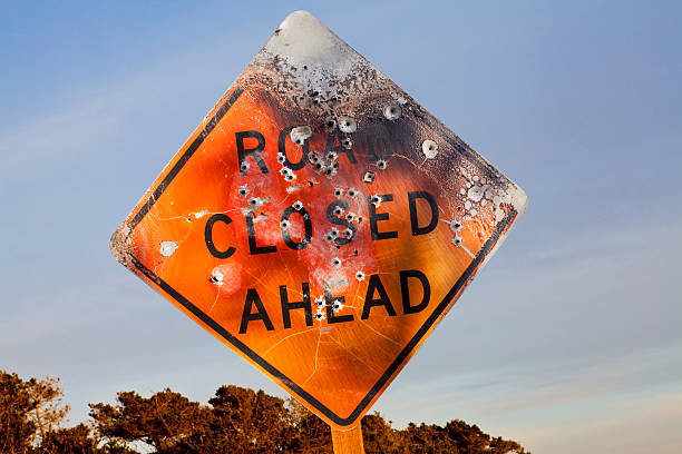 Road Closed Ahead sign full of bullet holes stock photo