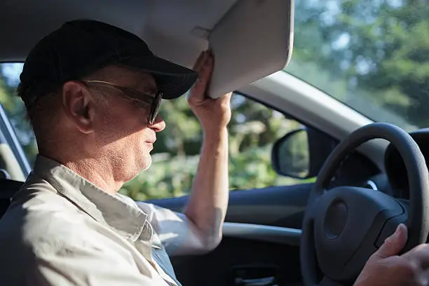 Side view of an old man at the wheel trying to hide himself from the sun with a sun visor