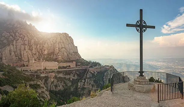 Christian cross from Montserrat Mountain viewpoint at sunset. View to the Monserrat Monastary  in the mountains. Famous Monastary near Barcelona, Catalonia, Spain.