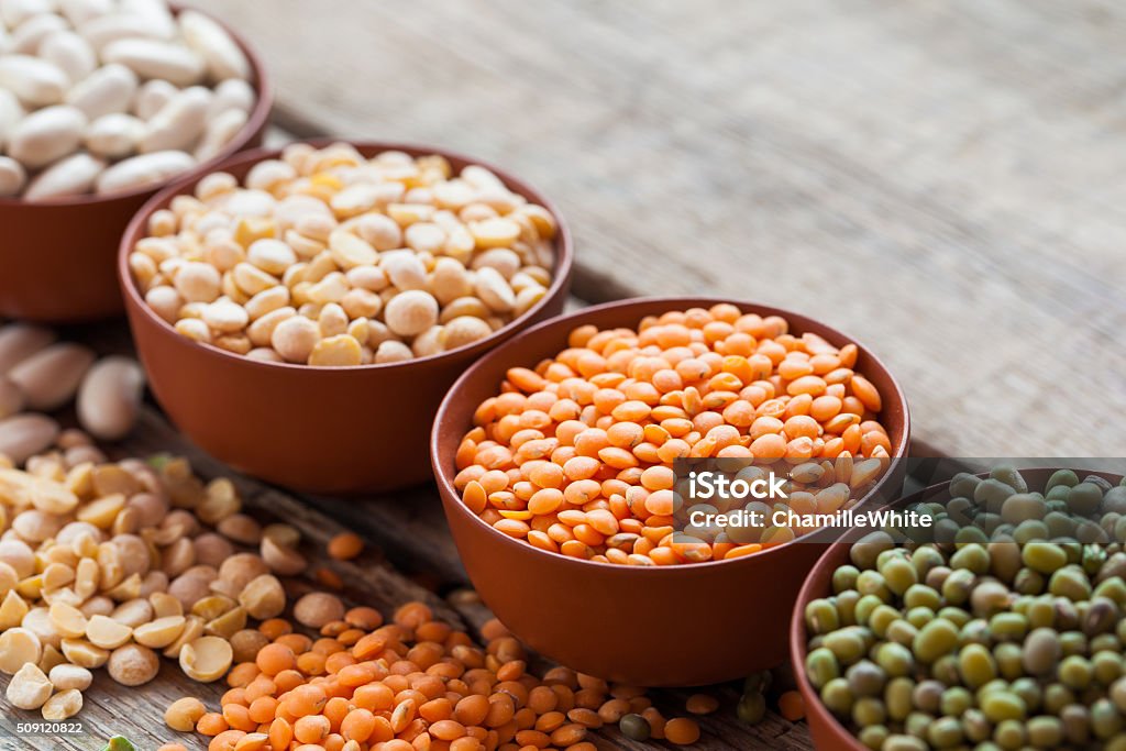 Bowls of cereal grain Bowls of cereal grains: red lentils, green mung, corn, beans and peas on wooden kitchen table. Selective focus. Legume Family Stock Photo