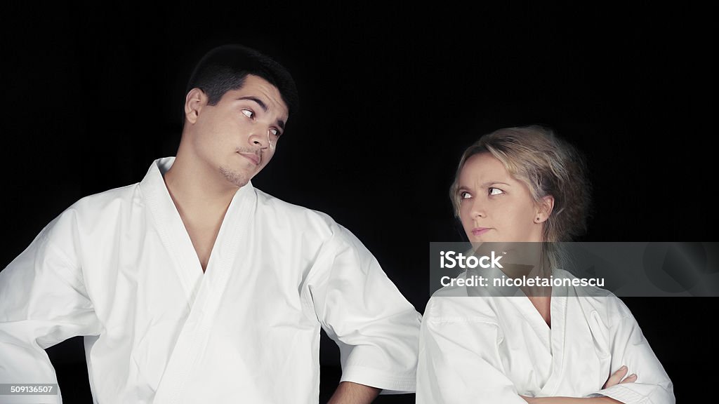 Karate Couple Wearing Kimonos Standing Together Young couple wearing kimonos standing next to each other with funny expressions, on a dark background Affectionate Stock Photo